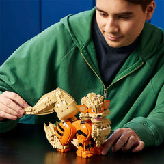 A person in a green hoodie plays with a toy fox built from beige and orange blocks on a dark table against a blue background.