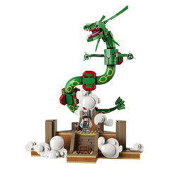 A green dragon toy building block set with a small character minifigure, standing on a brown platform with white cloud pieces, isolated on a white background.