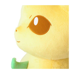 Close-up of a yellow plush toy with a large brown embroidered eye, a small stitched smile, and a green fabric detail at the bottom left, shown on a plain white background.