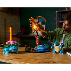 Man holding a Charizard toy with other Pokémon models on a table.